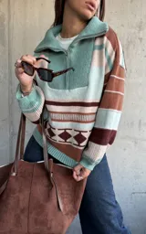 Sweater de tejido de punto con diseño a rayas horizontales y patrón geométrico en tonos verde, marrón y beige. Presenta cuello alto con cierre frontal, mangas largas abullonadas con puños ajustados y corte holgado.