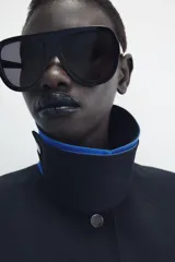 Chaqueta de Zara Woman Collection color negro, de cuello con solapa y manga larga. Cuenta con bolsillos delanteros ocultos en las costuras, cierre frontal con botones metálicos a presión y detalle de diseño asimétrico en azul en el cuello.
