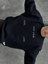 Buzo negro de corte holgado con cuello redondo y puños acanalados. Estampado frontal con la palabra "OSTEN" y la frase "NOT WHERE YOU'RE FROM A MINDSET OF BECOMING" en color blanco.