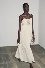Vestido largo color crudo, de algodón, con tirantes finos y escote recto. Presenta detalle de crochet en la parte superior.