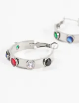 Aros tipo argolla de acero quirúrgico hipoalergénico color plateado, con strass incrustados de colores azul, rojo, blanco, negro y verde.