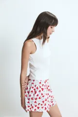 Pijama compuesto por una musculosa blanca de cuello redondo con pequeño bordado en el pecho y un short estampado con corazones rojos y texto sobre fondo blanco, con cintura elástica.