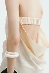 Top strapless de satén color beige, con diseño ceñido, drapeado lateral en la cintura y bajo asimétrico.