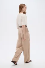 Pantalón de lyocell color beige, de tiro alto, corte ancho y diseño plisado con bolsillos laterales.