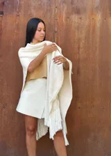 Ruana tejida de lana en color crudo, con diseño de flecos en los bordes. Es una prenda versátil y abrigada, ideal para complementar diversos looks.