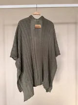 Ruana tejida de algodón con hilo lurex en punto jersey, color azul, con diseño amplio y detalle de etiqueta de cuerina en la parte posterior.