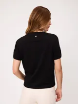 Remera blanca de manga corta con vuelta en los puños y detalle de botón dorado. Presenta cuello redondo y corte recto.
