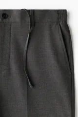 Pantalón de corte relajado en color gris oscuro, con cintura elástica, cierre de botón y cordón de ajuste oculto. Presenta raya marcada en las piernas, bolsillos laterales al bies y bolsillos traseros ribeteados con botón.