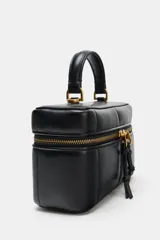 Bolso tipo vanity de estructura rígida y diseño acolchado con pespuntes. Cuenta con asa de mano superior y una cadena decorativa dorada con charms colgantes. Incluye cierre de doble cremallera y correa bandolera ajustable y extraíble.