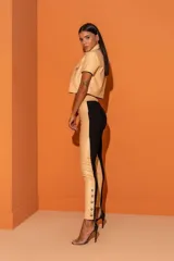 Pantalón de cuero sintético color beige, con cintura elástica, cierre frontal con cremallera y botones decorativos en los tobillos.