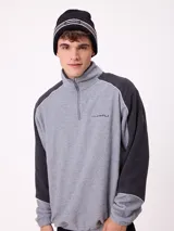 Gorro tipo beanie de punto color negro, con franja horizontal gris y blanca, y logo de la marca bordado en el frente.