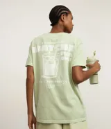 Remera de manga corta, cuello redondo y calce oversized, color verde claro con efecto lavado. Presenta un estampado serigráfico en la espalda con un vaso de bebida helada y texto que dice "i'm powered by MATCHA FUEL ONLY daily clean energy CLUB".