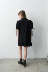 Vestido corto negro de broderie con cartera de botones asimétrica, mangas cortas abullonadas con lazo y volado en el ruedo.