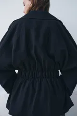 Trench corto de Zara, confeccionado en mezcla de lyocell, color verde militar. Presenta cuello solapa, manga larga con hombro caído y puños con trabilla. Incluye bolsillos delanteros de plastrón, cierre frontal cruzado con botón y cinturón de lazada en el mismo tejido.