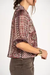 Blusa de manga corta con estampado estilo paisley en tonos burdeos, verde y crudo, escote en V con apliques de lentejuelas doradas y diseño holgado.