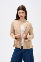 Saco de punto color gris, con cuello redondo, cierre frontal con botones y detalle de volados en la tapeta y el ruedo. Presenta mangas largas con puños acampanados.