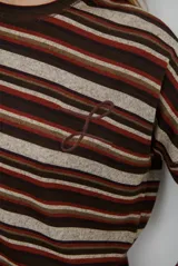 Remera de manga larga con diseño de rayas horizontales en tonos marrones, beige y rojizos. Presenta cuello redondo y un detalle bordado en el pecho.