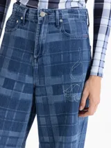Pantalón de jean de tiro medio y pierna amplia con diseño de cuadros estampados y detalles bordados de flores en contraste. Presenta bolsillos clásicos, cierre frontal con botón metálico y recortes estructurales en las piernas.
