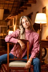 Blusa rosa de algodón con cuello alto y mangas largas abullonadas. Presenta detalles de cinta negra en el cuello y los puños, hombros con diseño princesa y cierre de lágrima con botón forrado en la parte posterior del cuello.