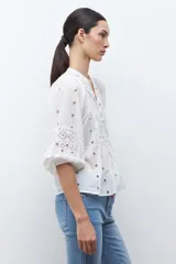 Blusa color verde oliva de manga 3/4 con volumen, cuello mao con abertura en V y botones. Presenta bordados y detalles de broderie calado en el canesú frontal y en las mangas. El cuerpo tiene un corte peplum con frunces.