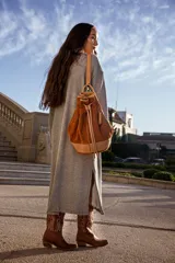 Mochila tipo bucket color marrón tostado, confeccionada en gamuza con detalles en cuero color beige. Cuenta con bolsillo exterior con cierre, bolsillo interior con cierre, llavero interno, asa de mano y correa extraíble y regulable para usar como mochila o bolso de hombro.