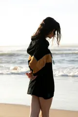 Hoodie de tela de toalla color azul, con cuello alto y cierre frontal de cremallera amarilla. Presenta bloques de color rojo en los hombros y detalles de ribetes amarillos. Tiene un bolsillo tipo canguro y un parche decorativo en el pecho.