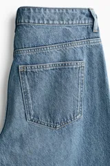 Jean de tiro alto y corte baggy, confeccionado en denim de algodón rígido en tono azul medio con efecto deslavado. Presenta diseño de cinco bolsillos, trabillas para cinto y cierre frontal con botón y cremallera.