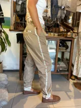 Bombacha de campo color beige, confeccionada en acrocel de algodón, con corte unisex de tiro medio. Presenta detalles de tela estampada con diseño floreado en la cintura, bolsillos, puños y una franja lateral a lo largo de la pierna. Cuenta con cierre reforzado y botón de madera.