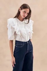 Blusa blanca de algodón con bordado floral, cuello redondo, manga corta con volados y cierre frontal con botones.