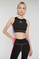 Crop top deportivo negro sin mangas, con banda lateral color block en violeta y naranja, logo estampado en el frente y calce ajustado.