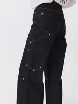 Pantalón de tiro medio y pierna ancha confeccionado en denim de algodón grueso. Presenta un diseño a rayas verticales en tonos azul y celeste, con costuras en contraste color rojo, bolsillos laterales tipo cargo y remaches metálicos.