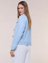 Campera de denim liviano azul, de corte clásico y silueta recta, con cuello camisero, cierre frontal con botones rústicos y bolsillos con solapa en el pecho.