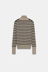 Jersey de punto liso en color beige, con cuello alto y manga larga con detalle de botones metálicos en los puños.
