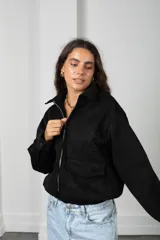 Campera de gamuza negra con cierre frontal, cuello camisero, bolsillos delanteros con solapa y puños con botón.