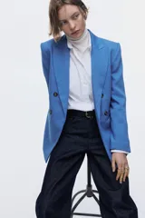 Blazer cruzado celeste de manga larga con solapas de pico, hombreras y bolsillos frontales con solapa. Presenta cierre de doble botonadura con botones oscuros y forro interior.