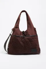 Bolso tipo tote de Bimba y Lola en color marrón, confeccionado en tejido técnico con un bolsillo frontal exterior cubierto por una red decorativa. Cuenta con asas superiores, correa ajustable extraíble y parche con logo de la marca en la parte inferior.
