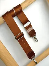 Correa ajustable para cartera confeccionada en cuero marrón con costuras a la vista y herrajes metálicos plateados.