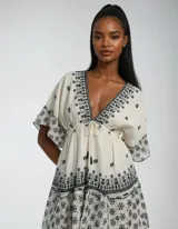 Vestido corto color crudo con bordado floral negro, escote en V, mangas 3/4 acampanadas y cintura ajustable con cordón.