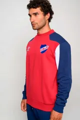 Buzo deportivo Umbro del Club Nacional de Football, color rojo con mangas azul marino y detalles blancos. Cuenta con cuello redondo y el logo de la marca y del club bordados en el pecho.