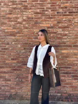 Bolso matero de cuero color chocolate con textura croco, asas cortas y detalle de costuras en los laterales. Incluye un dije con flecos en tonos beige y negro.