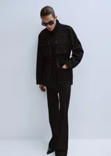 Parka de denim negro de corte largo, con cuello alto, cierre frontal oculto y múltiples bolsillos con solapa en el pecho y los costados. Cuenta con cordón ajustable en la cintura.
