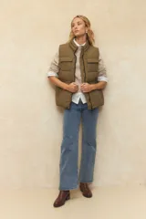 Chaleco puffer color crema, con cuello alto, cierre frontal y cuatro bolsillos con solapa. Cuenta con cintura ajustable con cordón.