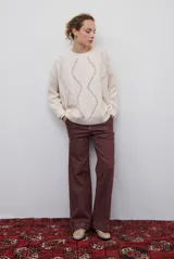 Buzo de punto color beige con diseño de trenzas y costuras decorativas en contraste que forman rombos. Presenta cuello redondo, mangas largas y puños acanalados.