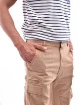 Bermuda tipo cargo color beige, con bolsillos laterales con cierre y bolsillos cargo en las piernas. Presenta cierre frontal con botón y presillas para cinturón.