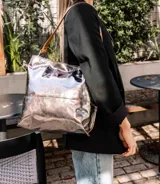 Bolso tipo hobo de cuero con acabado texturizado en tono beige claro, con correa de hombro en cuero liso color suela y herrajes metálicos en bronce envejecido.