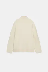 Jersey de punto liso color beige, con cuello subido y manga larga. Presenta acabados en rib en cuello, puños y ruedo.