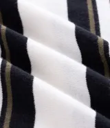 Remera boxy de punto listrado en blanco, negro y verde oliva, con cuello polo y abertura frontal con botones. Posee caída cómoda y textura suave.