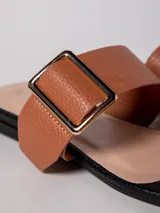 Sandalia baja negra de cuero sintético, con tira ancha sobre el empeine con hebilla metálica dorada y tira para el dedo.