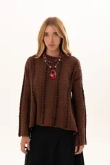 Buzo de tejido de punto color chocolate con diseño de trenzas verticales y detalles de costuras en contraste color negro. Presenta cuello redondo, mangas largas con terminación acampanada y aberturas laterales en el ruedo.