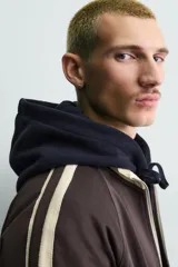 Sudadera de corte relajado en color azul marino con cuello alto y cierre frontal de cremallera. Presenta bandas laterales en color crema a contraste que recorren las mangas, puños y bajo en tejido rib, y bolsillos laterales de vivo.